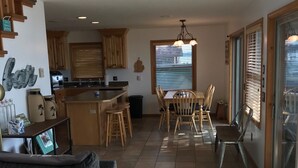 A spacious living area with a sofa, a dining table with chairs, a kitchen area with wooden cabinets, and a large window allowing natural light. - East Twin Lake House - 2 Minutes to town (Lewiston)