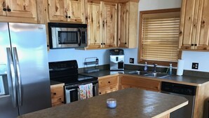 A kitchen with wooden cabinets, stainless steel appliances, a large island with stools, and a tiled floor. - East Twin Lake House - 2 Minutes to town (Lewiston)