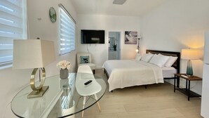 Una habitación de hotel moderna con cama, mesita de noche, lámpara y una mesa de vidrio con un florero.