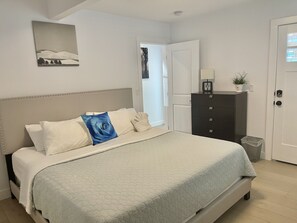 Une chambre à coucher avec un lit, une commode, une porte et un tableau accroché au mur.