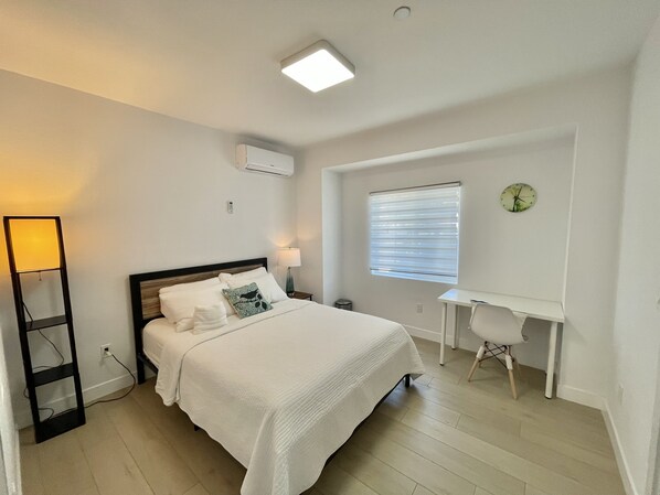 A neatly arranged bedroom with a bed, bedside table, lamp, and a desk with a chair.