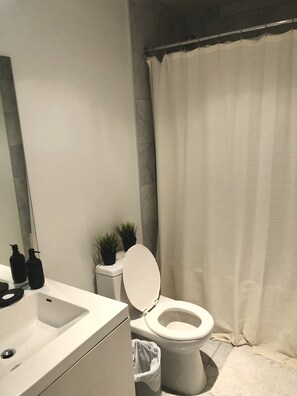 Bathroom features a toilet, sink, and shower, with two potted plants nearby.