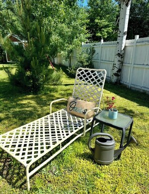A metal garden chair with a lattice backrest and a cushion labeled 'Oasis,' a small metal table with a plant, and a metal watering can. - Charming Red House • Private Yard • Fire Pit (Marquette)