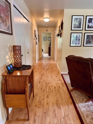A hallway with wooden flooring, a desk with a tablet, framed pictures on the walls, and a couch.