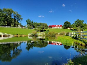 A serene lakeside scene with a red-roofed building, white fences, and lush greenery. - Minutes from New River Gorge!  Country setting - great for families and friends! (Fayetteville)