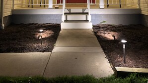 Una casa con una porta rossa, due finestre, un portico con sedie e un ingresso ben illuminato.