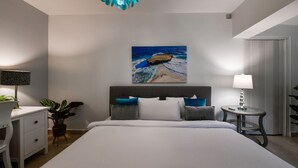 Een slaapkamer met een bed, een bureau, een stoel, een lamp en een schilderij van een strand.