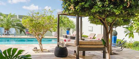 A poolside area with lounge chairs, a pergola, and a small tree.