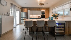 Een moderne keuken met een centraal eiland, barstoelen, een inbouwoven en een koelkast.