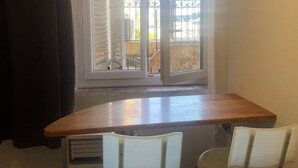 Una pequeña cocina americana con ventana que da a un balcón. Hay dos sillas blancas y una mesa de madera.
