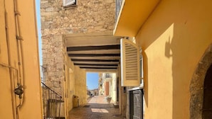 Un estrecho callejón con suelo de piedra, un edificio amarillo a la derecha y una pared de piedra a la izquierda.