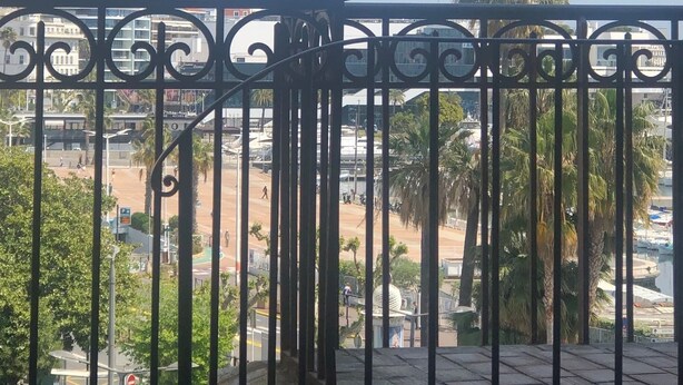 Balcón con baranda de metal que ofrece vista a un paisaje urbano con edificios, palmeras y cielo despejado.