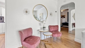 Una sala moderna con dos sillones de terciopelo rosa, un espejo redondo y una mesita blanca.
