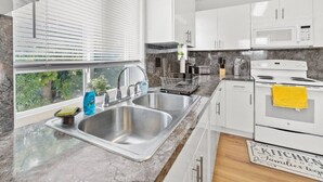 Una cocina moderna con armarios blancos, un lavamanos de acero inoxidable, un microondas y una estufa.