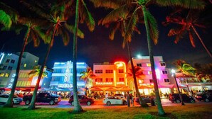 Un hotel muy iluminado con un letrero de neón, palmeras y una calle concurrida en la noche.