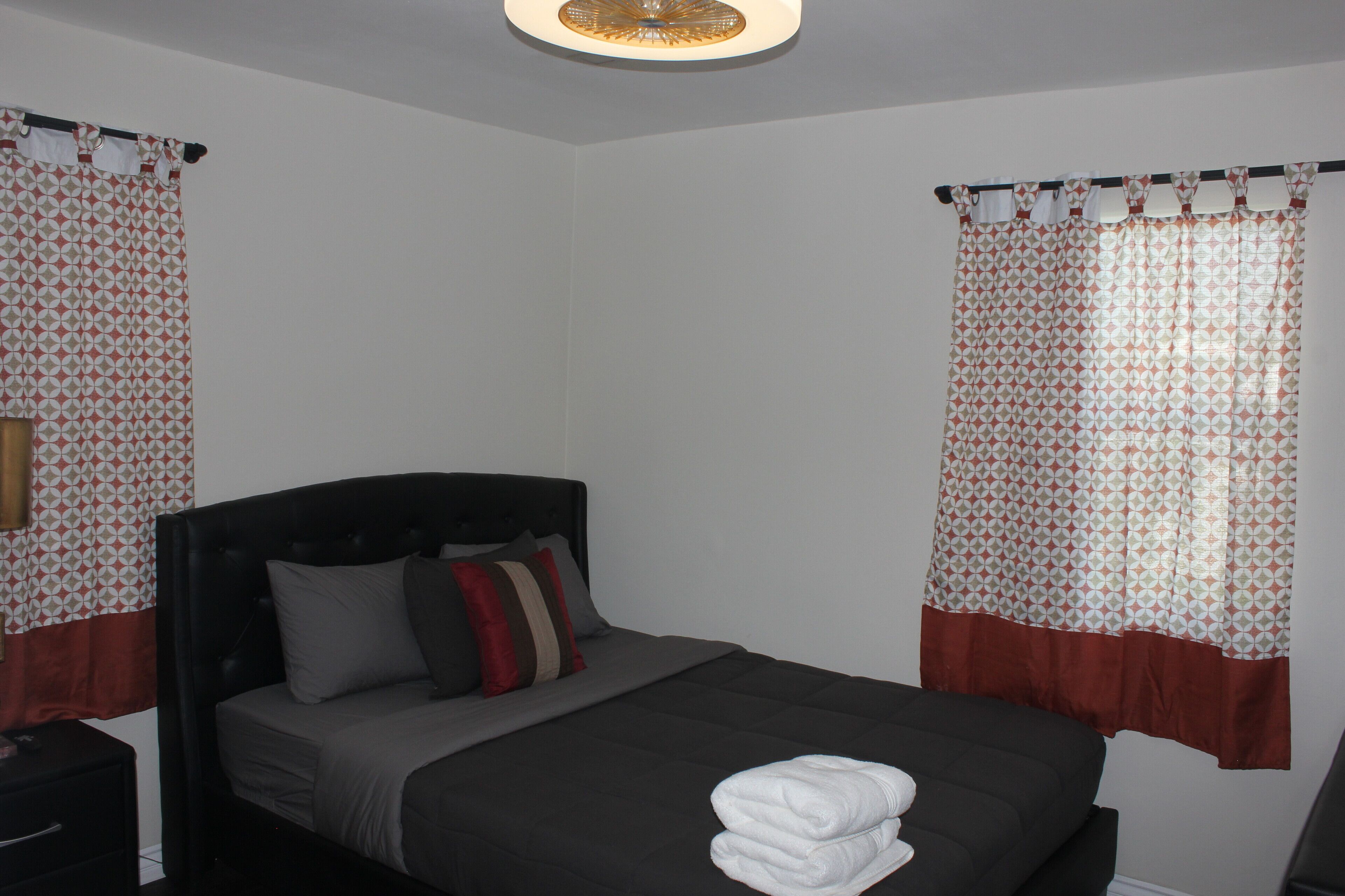 Cama bem arrumada com cabeceira escura, mesa de cabeceira e luminária fixada na parede.