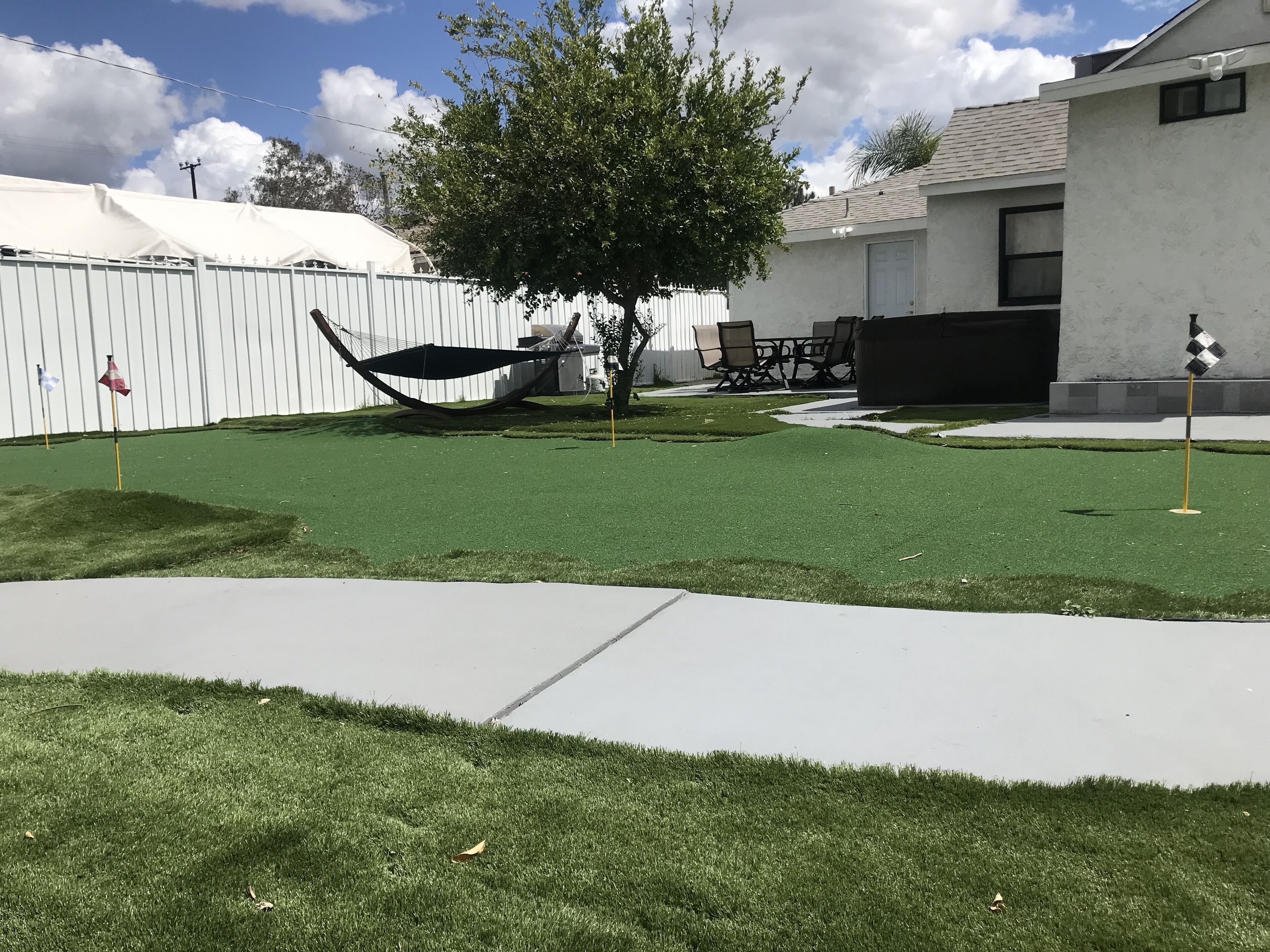 A backyard with artificial grass, a hammock, a tree, and a patio area with chairs and a table.