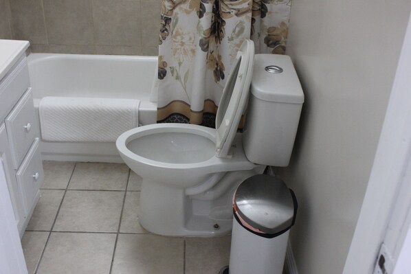 A bathroom with a toilet, a bidet, a trash can, and a bathtub.