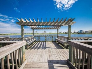 Un molo in legno conduce a una zona riparata con panchine, affacciata su uno specchio d'acqua.