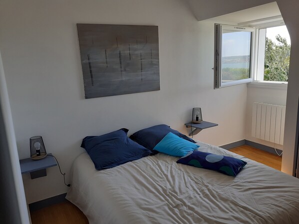 A bedroom with a bed, a nightstand, a wall-mounted lamp, a radiator, and a window with a view.