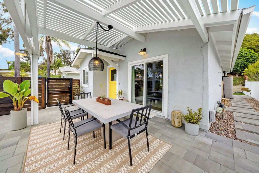 A covered patio area with a table and chairs, potted plants, and a pergola structure.