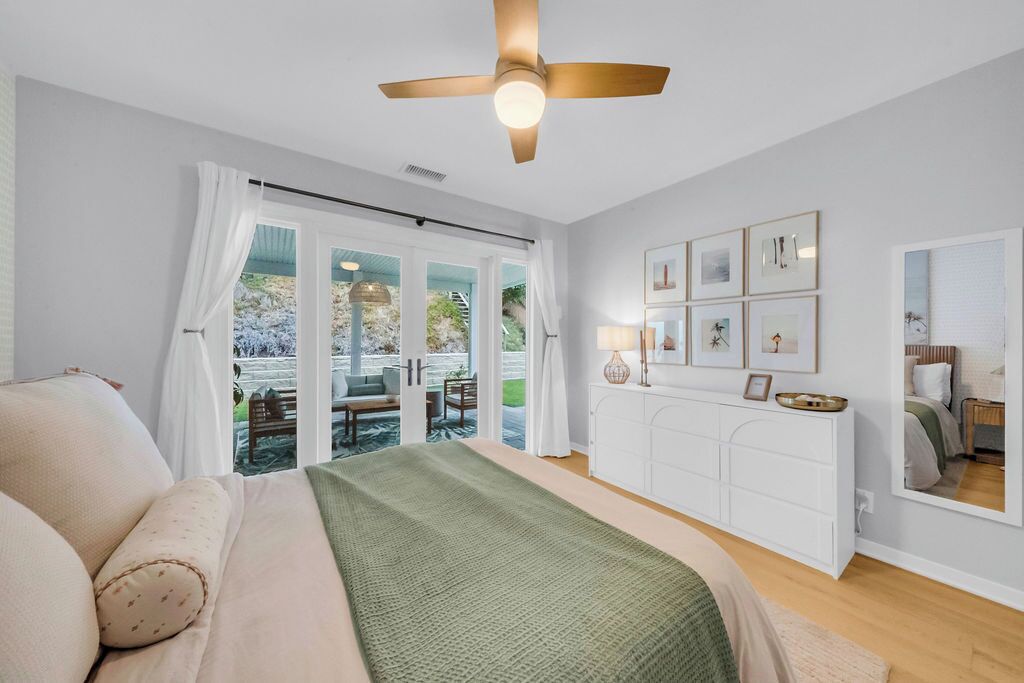 A bedroom with a bed, a ceiling fan, a white dresser, and a large window with curtains.