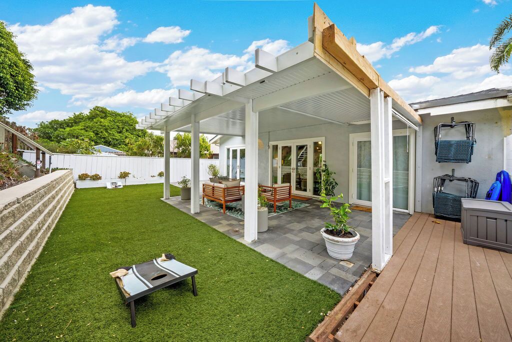A covered patio area with a wooden deck, a small lawn, and a seating area with a bench and table.