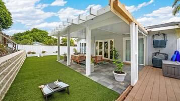 A covered patio area with a wooden deck, a small lawn, and a seating area with a bench and table.