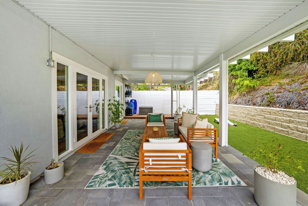 A covered patio area with a seating arrangement, potted plants, and a view of the surrounding landscape.