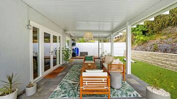 A covered patio area with a seating arrangement, potted plants, and a view of the surrounding landscape.