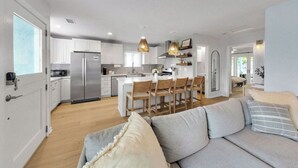 Une cuisine moderne avec des meubles blancs, un réfrigérateur en acier inoxydable et un coin repas doté de chaises en bois.