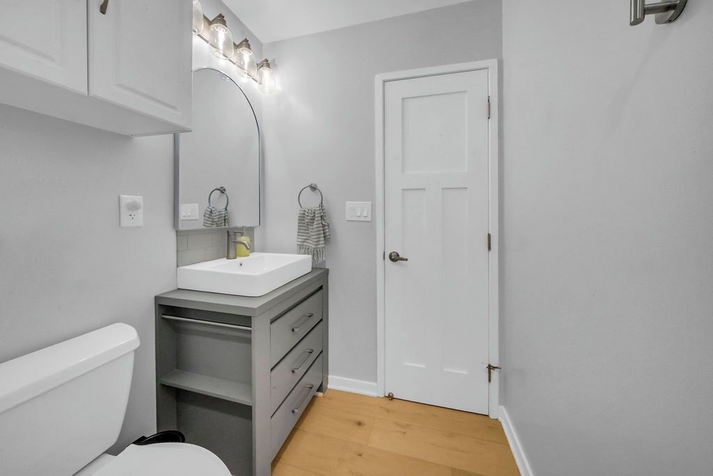 Ein Badezimmer mit einer weißen Toilette, einem grauen Waschtisch mit Spiegel und einer weißen Tür.