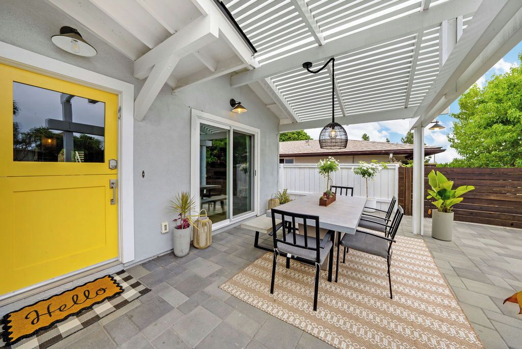 A covered patio with a table and chairs, a yellow door, and a 'Hello' mat.