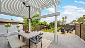 Une terrasse avec une table et des chaises, une pergola et une vue sur le jardin arrière.