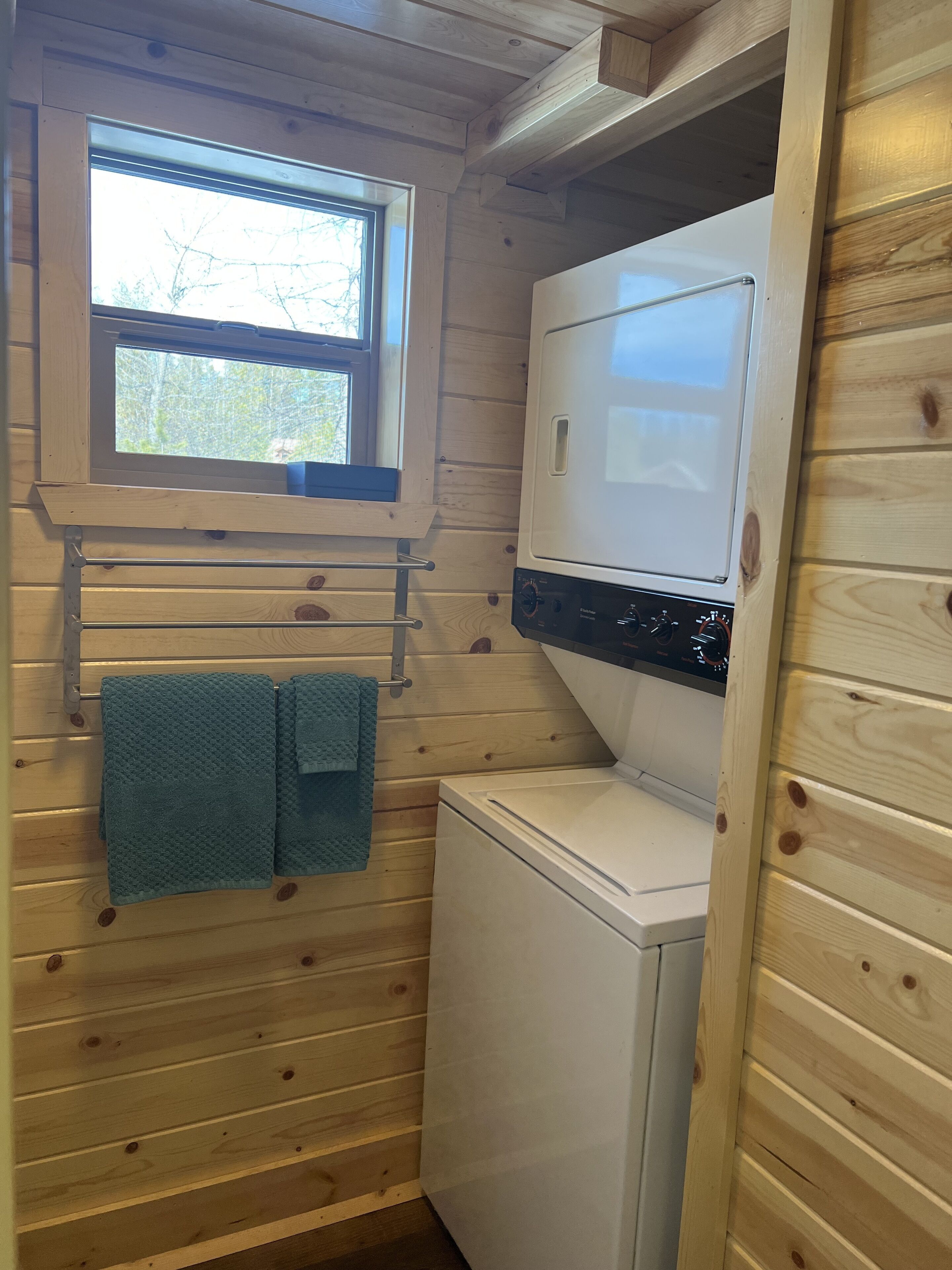 A compact laundry room with wooden walls, a window, and a washing machine.
