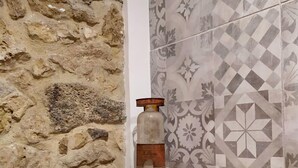 Une pièce avec un mur en pierre, un mur recouvert de carreaux décoratifs et une étagère en bois sur laquelle se trouve une bouteille.