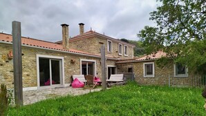 Une maison en pierre avec un toit recouvert de tuiles rouges, une cour gazonnée et une clôture en bois.