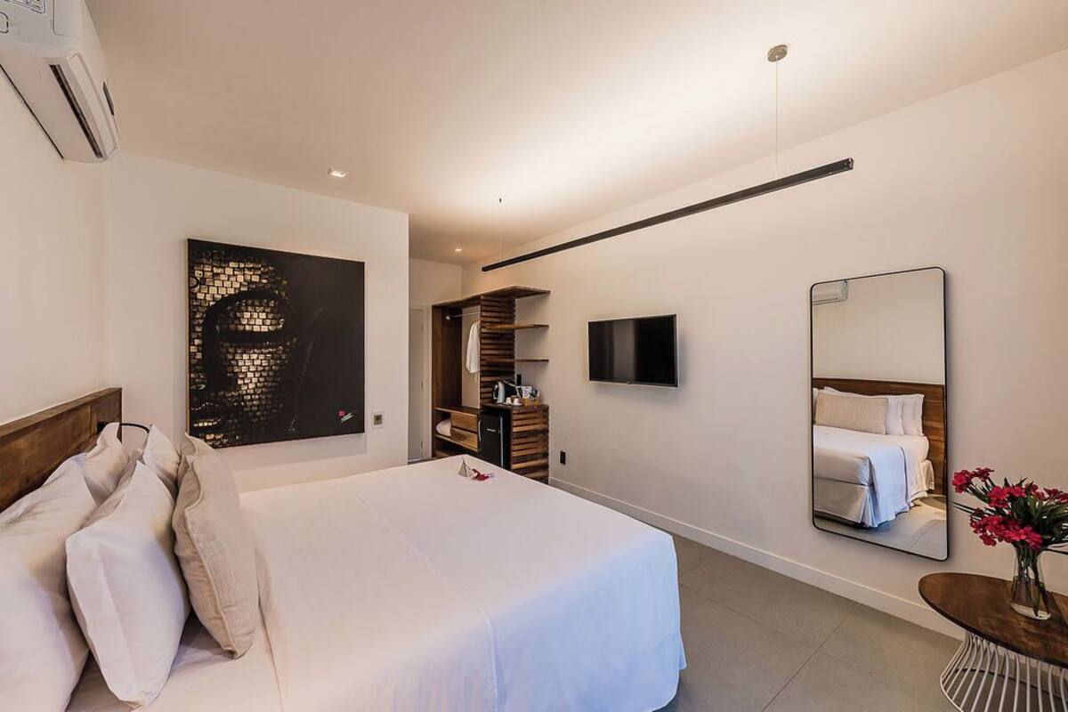 A modern hotel room with a large bed, a flat-screen TV, a mirror, and a wall-mounted artwork.