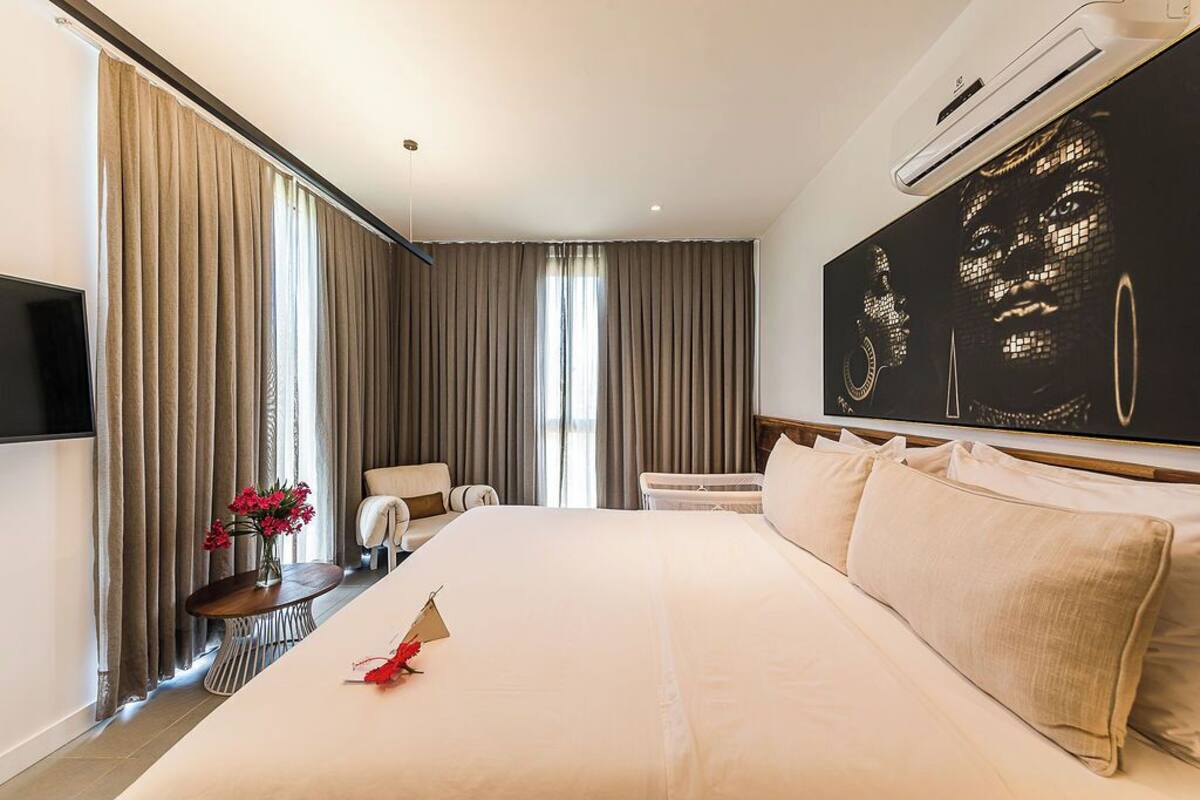A hotel room with a large bed, a flat-screen TV mounted on the wall, a large window with curtains, and a painting on the wall.