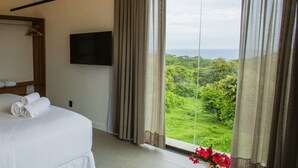 Quarto de hotel com cama, televisão de tela plana, janela grande com cortinas e vista para o verde.