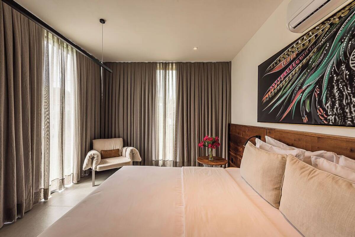 A hotel room with a large bed, a chair, a small table with a vase of flowers, and a painting on the wall.