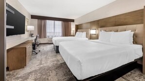 Habitación de hotel con dos camas, un escritorio, un televisor y un ventanal con cortinas.
