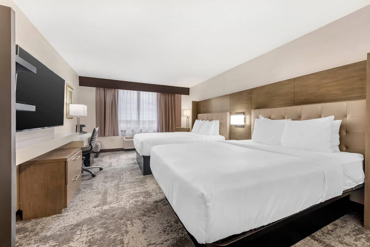 Habitación de hotel con dos camas, un escritorio, un televisor y un ventanal con cortinas.