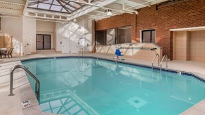 Una piscina interior con techo de tragaluces, pared de ladrillo y escalera de acceso.