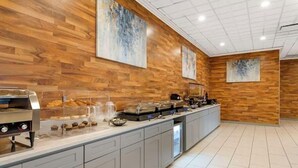 Una barra de desayuno con una máquina de café, un mostrador de comida y un lavabo.