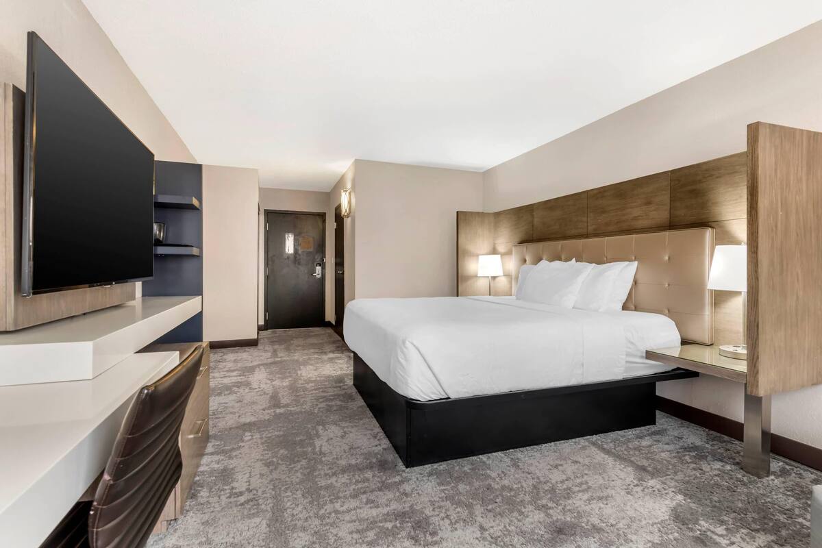 Una habitación de hotel moderna con una cama grande, un televisor de pantalla plana, un escritorio y una silla.