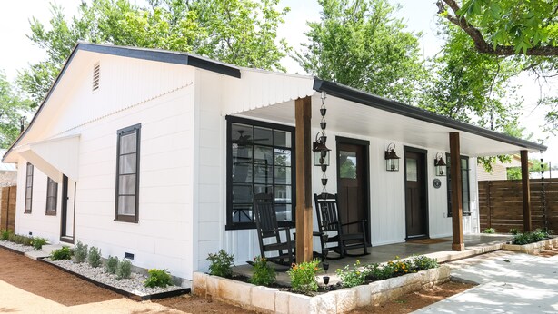 Een modern huis met een overdekte veranda, grote ramen en een kleine tuin.