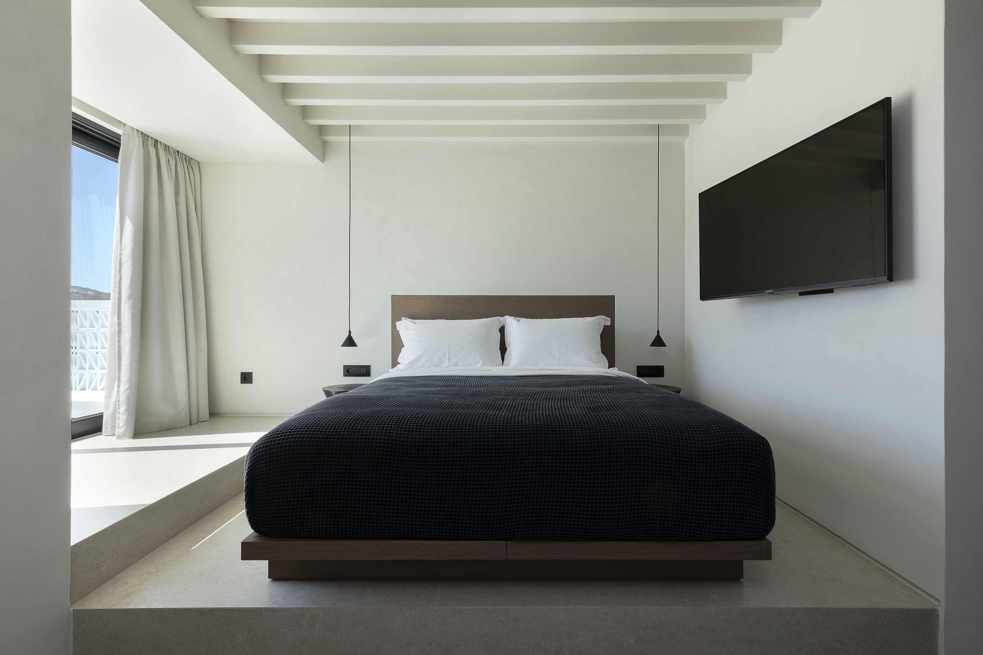 Un dormitorio moderno con una cama centrada bajo un techo de listones, un televisor de pantalla plana en la pared y una ventana con cortinas.