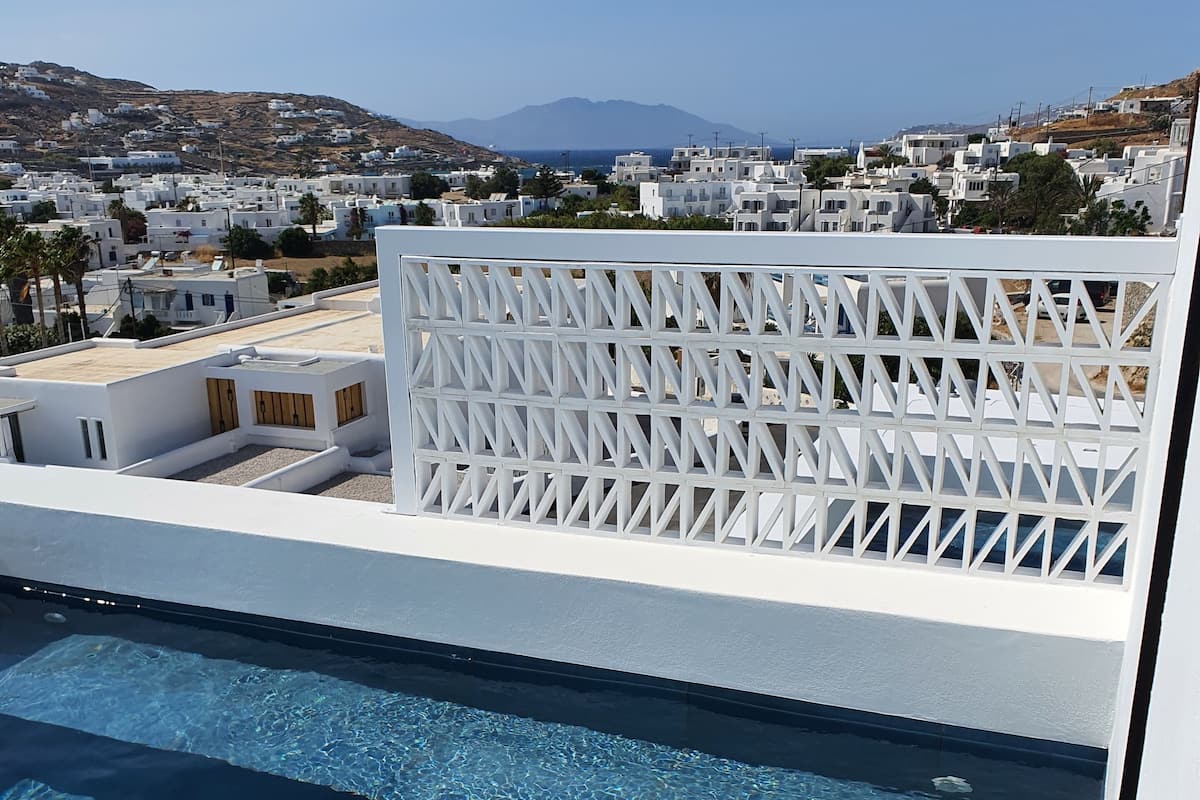 A rooftop pool with clear blue water, surrounded by white buildings and a view of distant mountains.