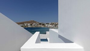 A white-walled building with a view of a coastal town and a hill in the background. - CUBIC Mykonos Seafront Design Suites (Mykonos)